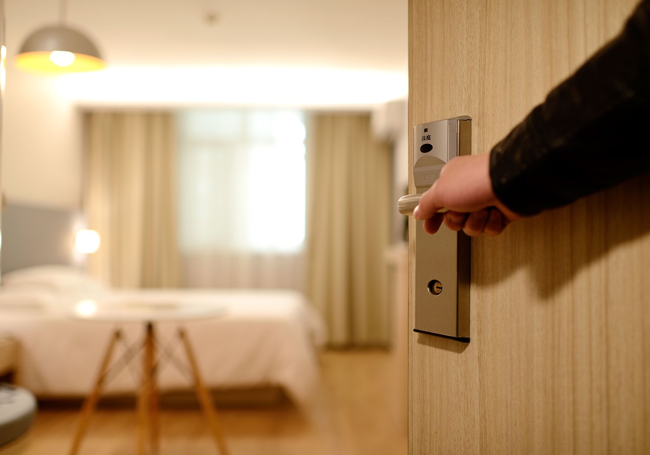 A man's hand on doorknob opening door to hotel room