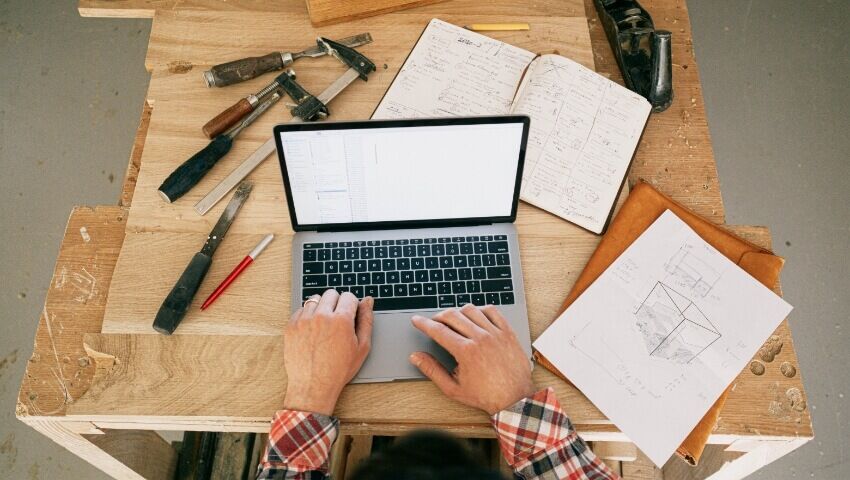 how-to-start-construction-business-canada desk with tools, hands on laptop working