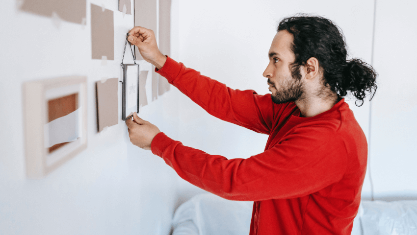 Man with red shirt hanging picture on the wall